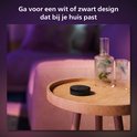 Zwarte Philips Hue Bridge op een houten tafel, met een zacht gekleurde bank op de achtergrond.