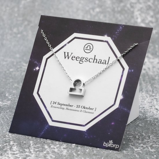 Collier argenté avec symbole Balance (Libra), présenté sur une carte sur le thème des étoiles.