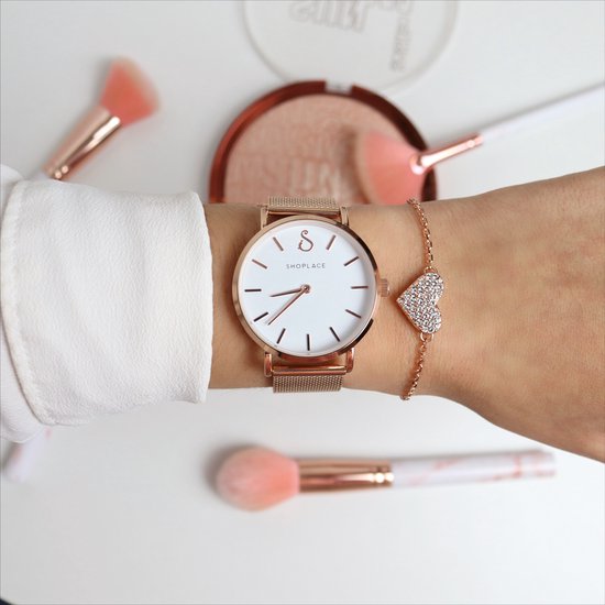 Damespols met roségouden armband met hartvormig bedeltje met kristallen, naast een horloge.