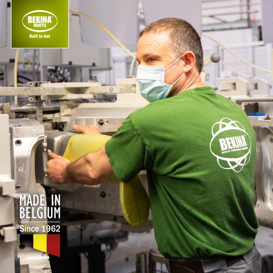 Man met mondkapje in groene T-shirt met logo van Bekina Boots, werkt aan machine in fabriek. "Made in Belgium Since 1962" logo.