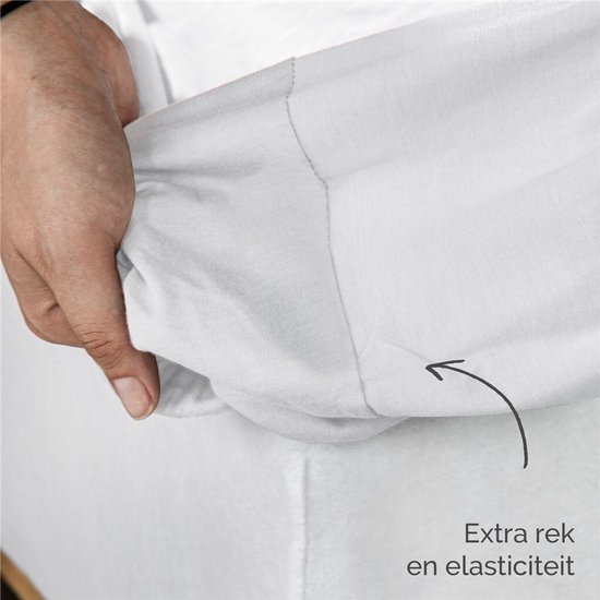 Een hand toont de extra rek en elasticiteit van een wit jersey hoeslaken.