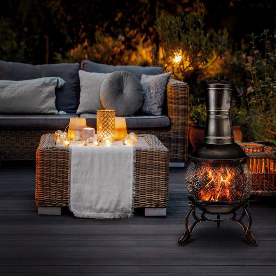 Verlichte terrasoven met brandende houtblokken, op een houten terras naast een loungeset en tafel.