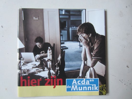 Hier zijn Acda en de Munnik. Twee mannen in zwart-wit, één zittend aan een bureau met laptop, de ander met gezicht in handen.