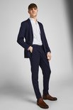 Man met donkerblauwe blazer en broek, wit overhemd en bruine schoenen.