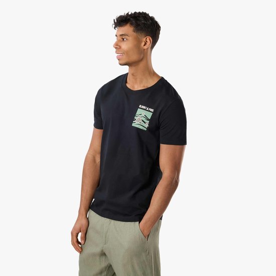 Man met zwarte t-shirt met kleine schildpaddenprint op de borst, gekleed in groene broek.