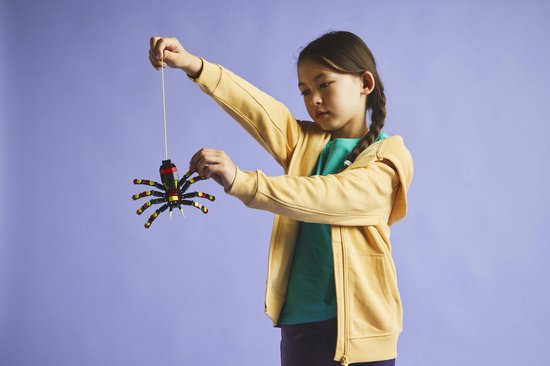 Een meisje in een gele hoodie speelt met een LEGO spin aan een geel koordje.