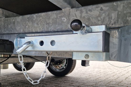 Zilverkleurige, kantelbare steunpoot met ketting en zwarte knop, gemonteerd aan de onderkant van een aanhanger.