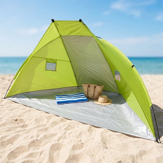 Groene strandtent op het zand, met handdoek, hoed en tas, aan zee.