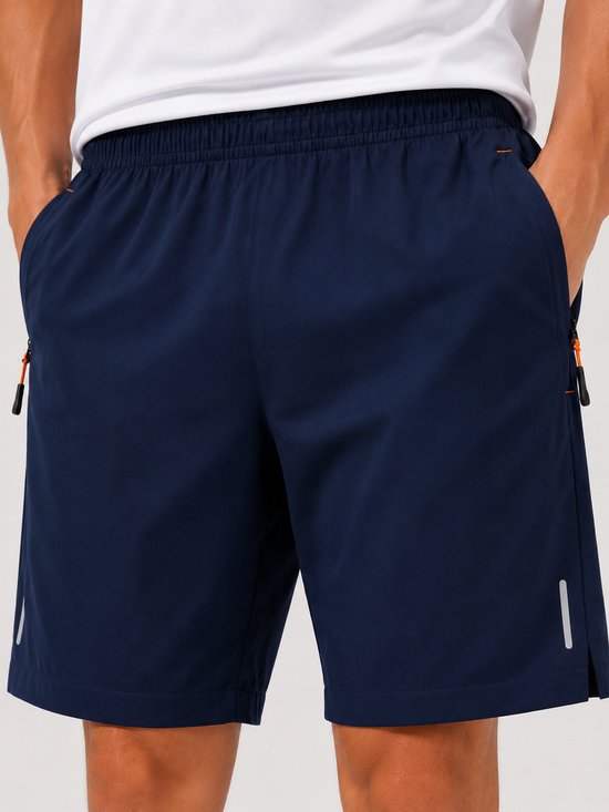 Donkerblauwe sportbroek met oranje rits detail en een reflecterende streep op de zoom.