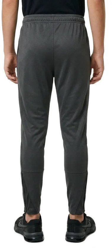 Jongen in een donkergrijze Nike trainingsbroek met rits aan de onderkant van de pijpen.