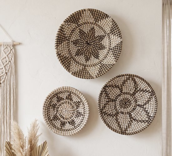 Drie zeegras wandschalen met zwart-wit spiraalpatroon aan een muur, naast een macramé wandkleed.
