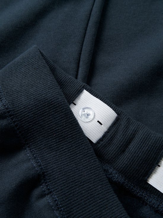 Sluiting van elastische tailleband met knopen, deel van een donkerblauwe joggingbroek.