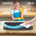 Vrouw met gele handschoenen en blauw schort die een zwarte grillplaat schoonspuit met een roze spray.