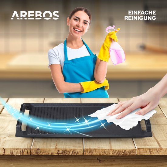 Vrouw met gele handschoenen en blauw schort die een zwarte grillplaat schoonspuit met een roze spray.