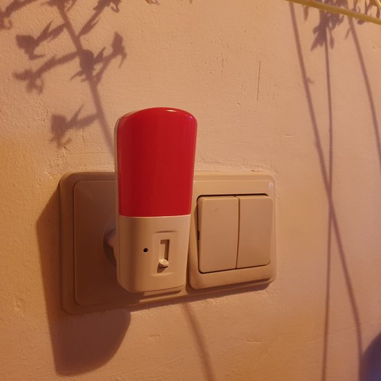 Een rood nachtlampje in een stopcontact met twee schakelaars, met schaduw van planten.