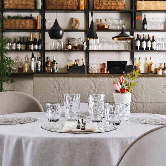 Table dressée avec quatre verres à motif ondulé, assiettes, couverts et fleurs.