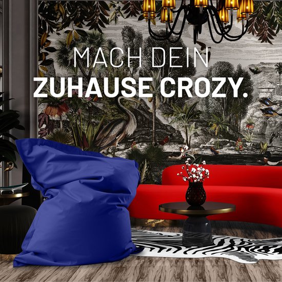 Een grote, donkerblauwe zitzak staat in een luxe woonkamer met een drukke wanddecoratie en een rode bank.