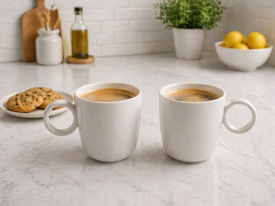 Deux tasses blanches avec du café et quelques biscuits dans une assiette sur un comptoir en marbre.