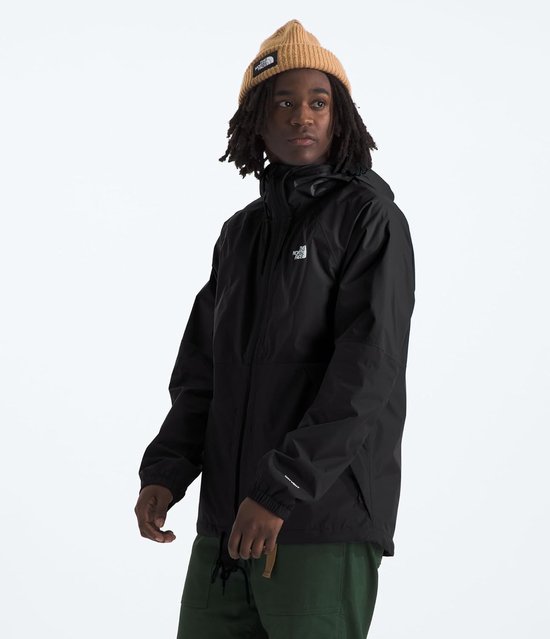 Jonge man in een zwarte The North Face outdoorjas met capuchon en bruine muts. Draagt een groene broek.