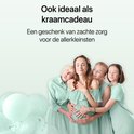 Een zwangere vrouw omarmd door drie vriendinnen, met ballonnen op de achtergrond, ideaal als kraamcadeau.