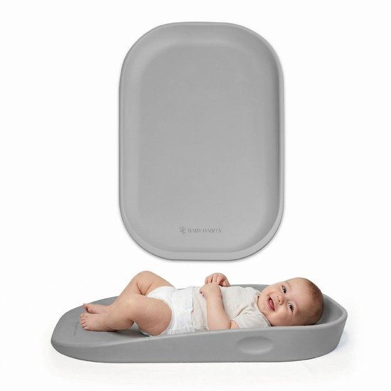 Grijs, ovaal baby verschoonkussen met Baby Habits logo. Baby ligt in een positie.