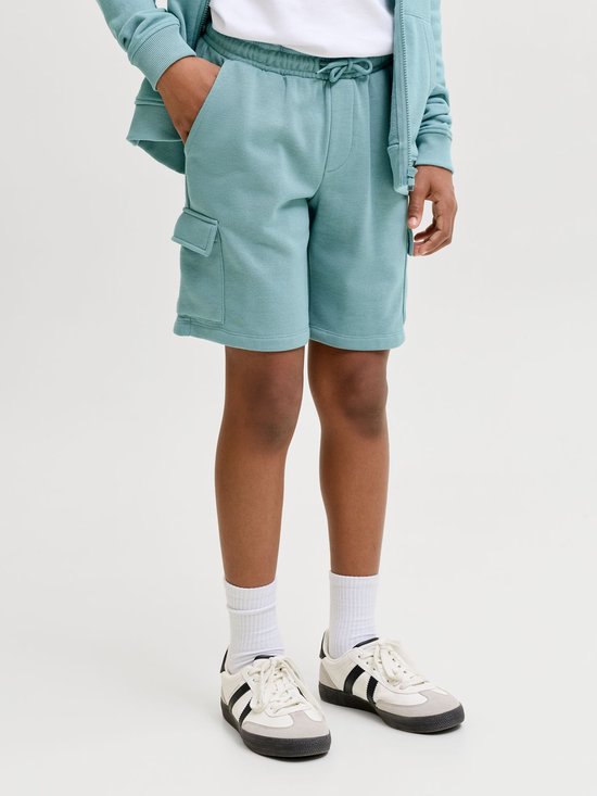 Jongenspootjes in een lichtgroene cargobroek, witte sokken en witte sneakers met zwarte strepen.