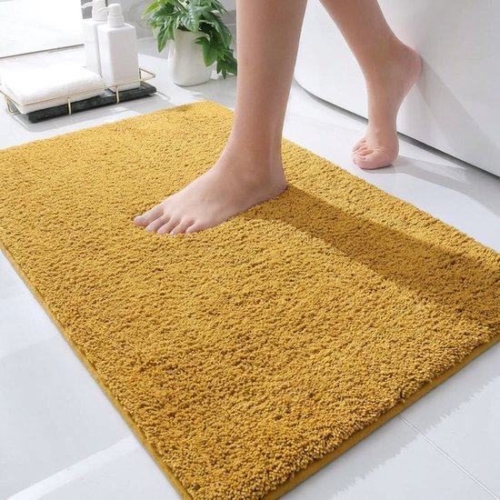 Een voet op een okergele badmat in een badkamer, bij een badkuip.