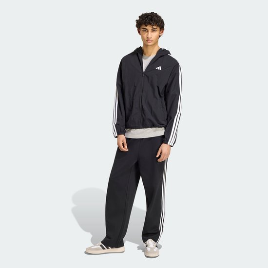 Model in zwart Adidas windjack met grijze onderlaag, zwarte broek en sneakers.