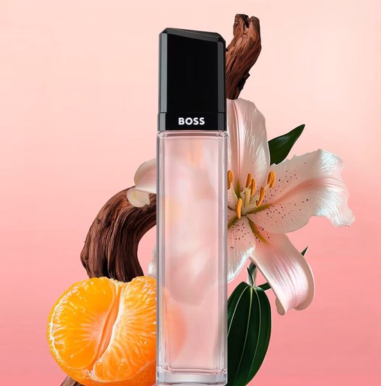 Hugo Boss Femme eau de parfum in een glazen fles met zwarte dop, omringd door een oranje partje, een witte lelie en een stuk hout.