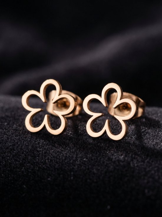 Gouden oorknopjes in de vorm van een opengewerkte bloem, op een zwarte achtergrond.