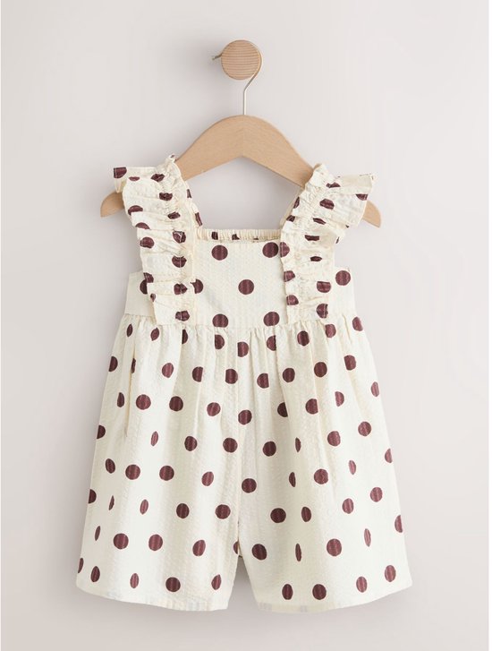 Crème kleurige romper met bruine polkadot print, ruches en smock, hangend aan een hanger.