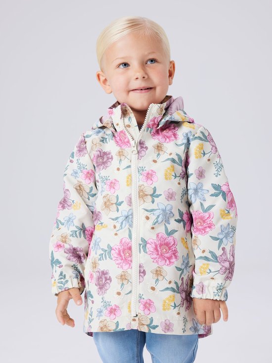 Meisje met blond haar draagt een beige jas met een bloemenprint in roze, paars, blauw en geel.