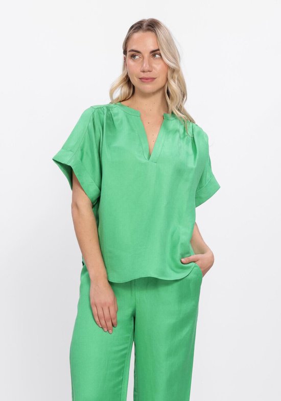 Model met groene blouse met V-hals en opgerolde mouwen, gecombineerd met een groene broek.
