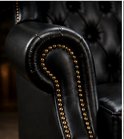 Detail van de armleuning van een zwarte leren wingback fauteuil met capitons en goudkleurige klinknagels.