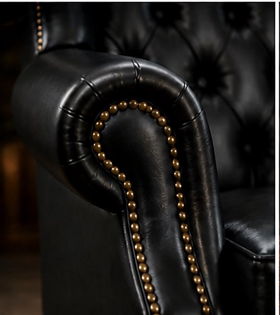 Detail van de armleuning van een zwarte leren wingback fauteuil met capitons en goudkleurige klinknagels.