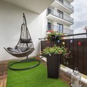 Balcon confortable avec fauteuil suspendu gris, jardinières et tapis d'herbe artificielle verte.