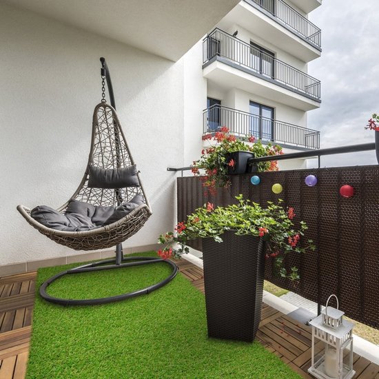 Balcon confortable avec fauteuil suspendu gris, jardinières et tapis d'herbe artificielle verte.