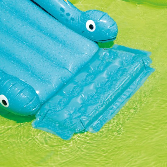 Detail van de blauwe dinosaurusglijbaan met een opblaasbare mat onderaan in het zwembad.