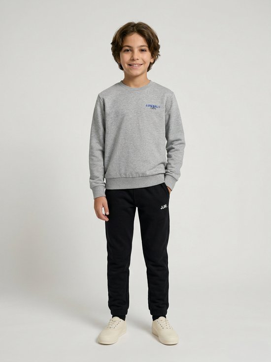Jongen draagt een grijze sweater met blauw logo en een zwarte joggingbroek met wit 'JJR.' logo.