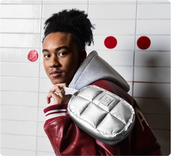 Jonge man met een bomberjack draagt een metallic zilveren Coze Mini tas.