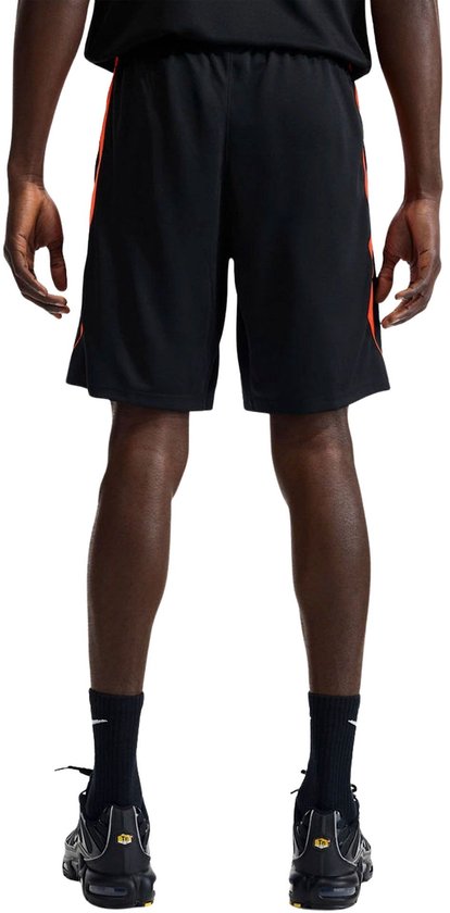Achterkant van een zwarte Nike voetbalshort met oranje accenten aan de zijkant.