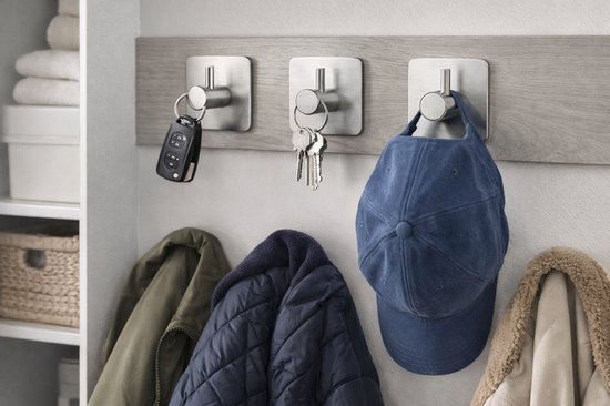 Zilverkleurige haken aan een houten achtergrond, met autosleutels, huissleutels, een blauwe pet en jassen eraan.