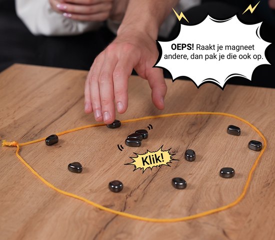 Close-up van handen die een spel met magneten spelen. Een hand reikt naar de magneten, een tekstballon zegt: 'OOPS! Raakt je magneet andere, dan pak je die ook op. Klik!'