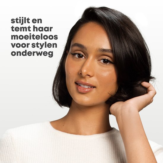 Een vrouw met kort, donker haar glimlacht en raakt haar haar aan.