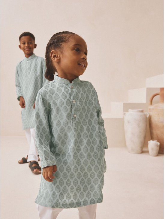 Jonge jongen in een lichtgroene kurta met bladpatroon en witte broek, kijkend naar rechts.
