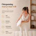 Een vrouw in beige kleding houdt een opgevouwen spijkermat in een draagtas vast.