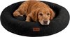Een bruine golden retriever ligt in een ronde, zwarte, pluche hondenmand met een bruin label.