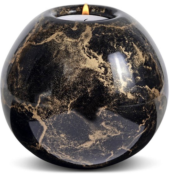Zwarte bolvormige urn met gouden marmering en een brandende kaars.