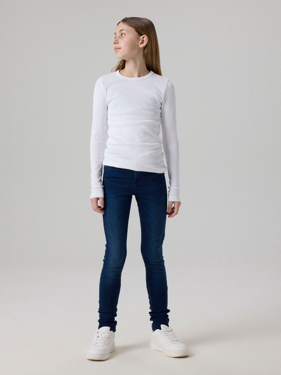Meisje staand in donkerblauwe skinny jeans en een witte top.