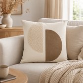 Crèmekleurig sierkussen met beige bouclé en bruine halve cirkels, op een lichte bank met gebreide deken.